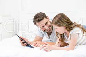 Father showing digital tablet to daughter on bed