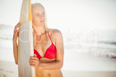 Woman in bikini standing with a surfboard on the beach