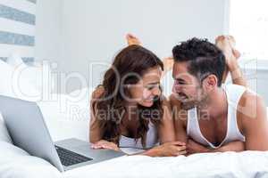 Smiling couple with laptop while lying under blanket