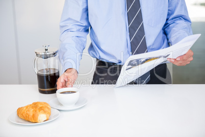 Businessman holding coffee cup and newspaper by table