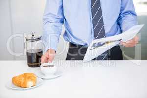 Businessman holding coffee cup and newspaper by table