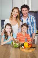 Portrait of happy family preparing vegetable salad