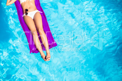 Woman in white bikini lying on air bed in pool