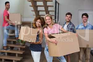 Cheerful young friends carrying carton in new house