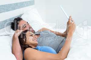 Happy young couple using tablet while lying on bed