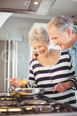 Happy senior man standing with wife cooking food at hob