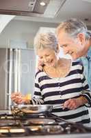 Happy senior man standing with wife cooking food at hob