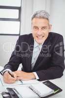 Happy businessman writing in spiral notebook