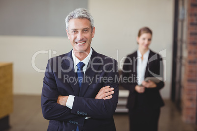 Businessman with arms crossed while colleague in background