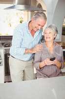 Happy senior man standing besides wife sitting in kitchen