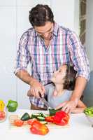 Smiling father teaching daughter to cut vegetable