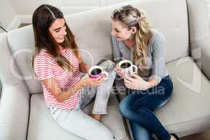 Female friends drinking coffee while sitting on sofa at home