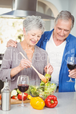 Senior woman preparing salad while man standing at counter
