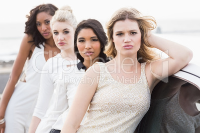Well dressed women posing leaning on a limousine