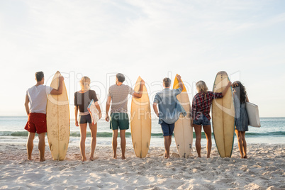 Happy friends standing in line with surfboards