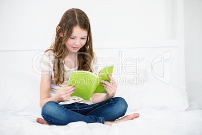 Girl reading book on bed at home