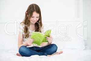 Girl reading book on bed at home