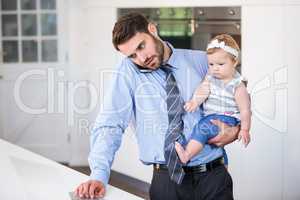 Businessman working on laptop while carrying daughter