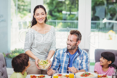 Smiling mother standing at dining table with family