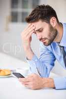 Tensed businessman using mobile phone by table
