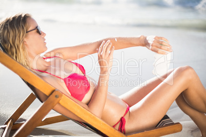 Woman sitting on armchair and applying sunscreen lotion