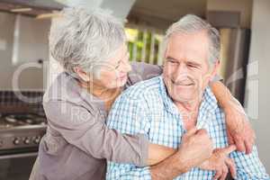 Cheerful senior couple embracing in kitchen