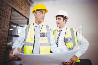 Male architects discussing while holding blueprint