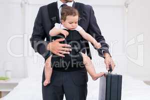 Midsection of father carrying baby while holding briefcase