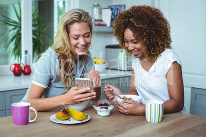 Female friends looking in cellphone during breakfast