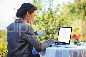 Pretty businesswoman using laptop and having coffee