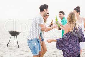 Group of friends dancing on the beach with beer bottles