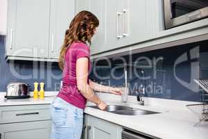 Woman filling water in glass from faucet