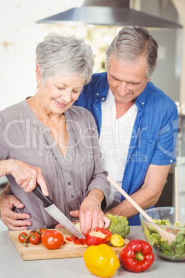 Senior woman cutting while man embracing in kitchen