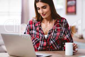 Smiling woman using laptop with coffee mug