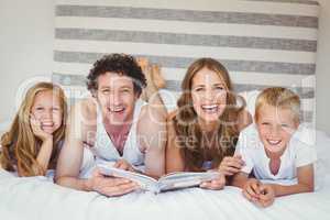 Portrait of happy family holding book on bed