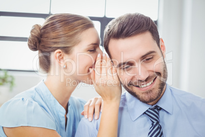 Happy businesswoman whispering to male colleague