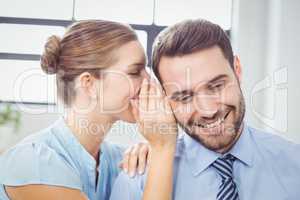 Happy businesswoman whispering to male colleague