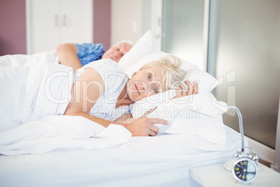 Thoughtful senior woman lying besides man on bed