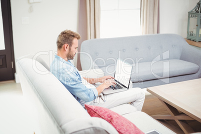 Man using laptop while sitting on sofa in living room