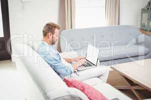 Man using laptop while sitting on sofa in living room