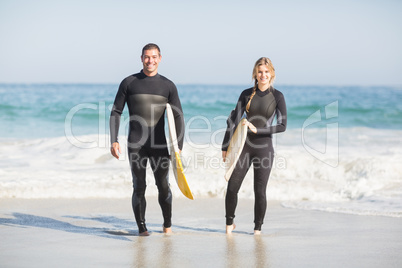 Portrait of couple with surfboard walking on the beach