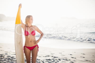 Woman in bikini standing with a surfboard on the beach