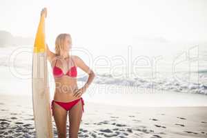 Woman in bikini standing with a surfboard on the beach