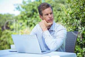 Thoughtful businessman using laptop with coffee