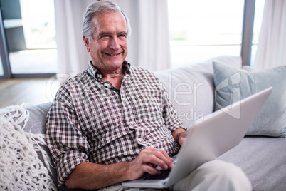 Portrait of senior man using laptop in living room