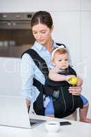 Woman carrying baby girl while working in laptop