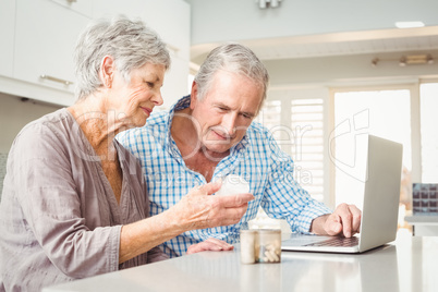 Senior woman showing pills to husband with laptop
