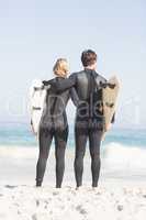 Rear view of couple with surfboard standing on the beach