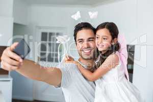 Smiling father taking self portrait with daughter in fairy costu
