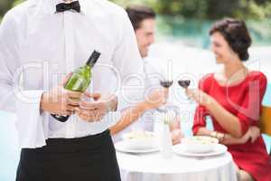 Midsection of waiter holding wine bottle